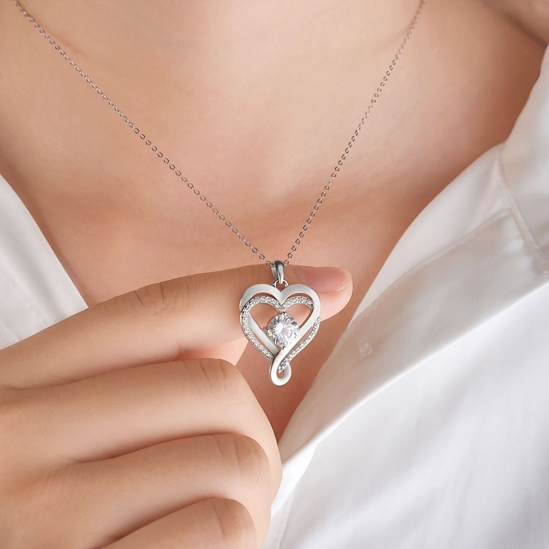Una persona con camisa blanca sostiene el collar plateado "A mi Esposa" con un colgante de piedras preciosas en forma de corazón, una opción elegante que resulta perfecta como regalo para parejas o accesorio chic para cualquier ocasión.